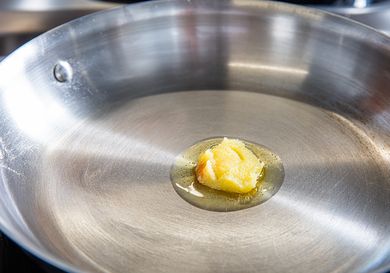 A piece of ghee melting in a stainless steel frying pan on a stove