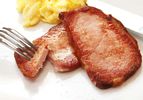 Closeup of browned slices of sous vide Canadian bacon, served on a white plate with scrambled eggs.