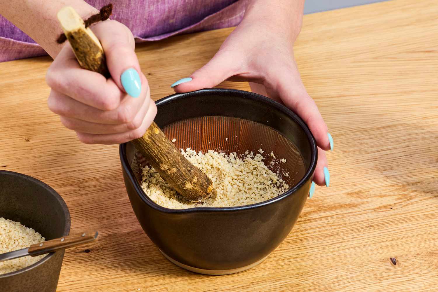A person crushing sesame seeds in a suribachi.