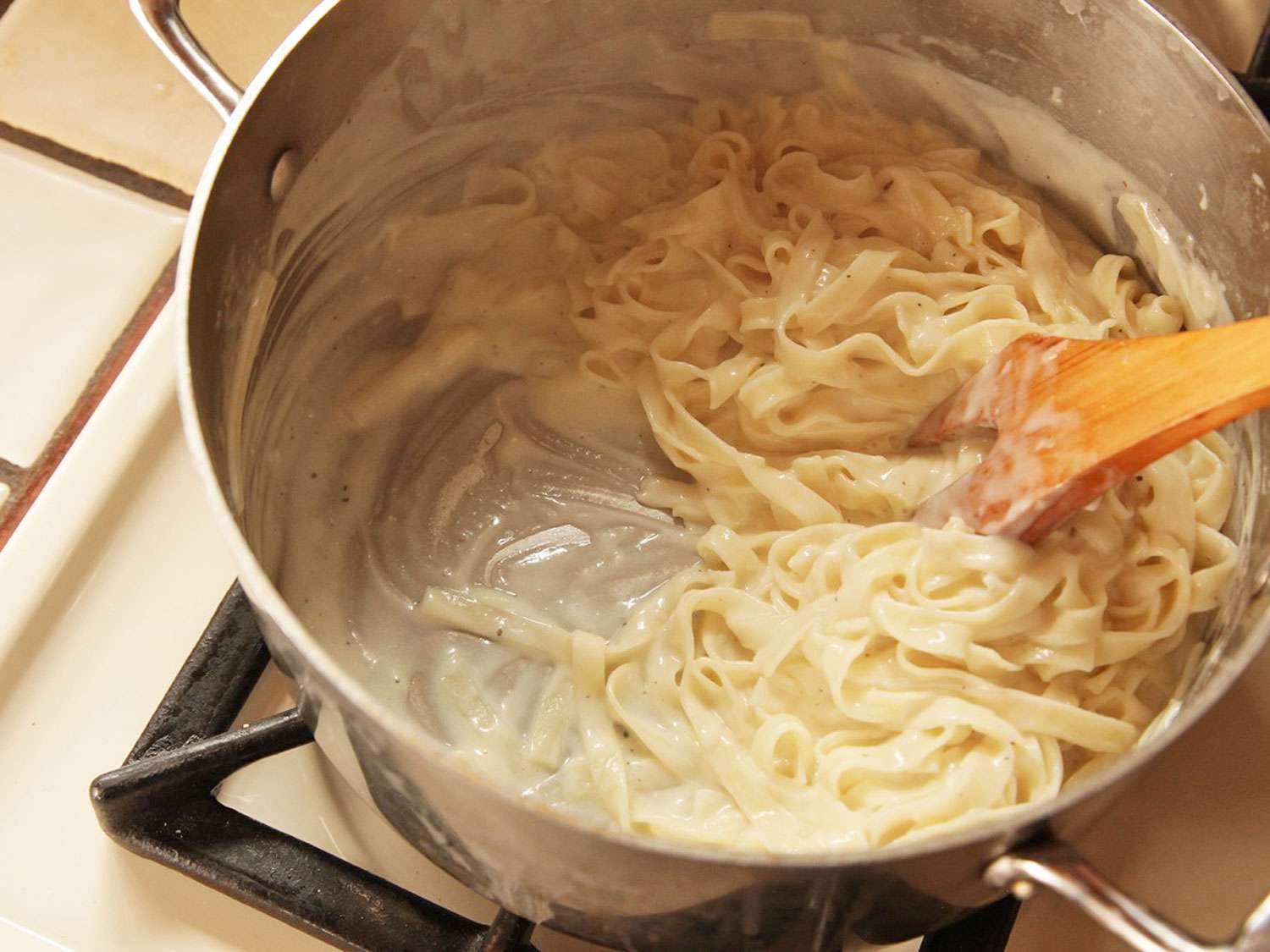 Stirring pasta and Alfredo sauce with a wooden spoon.