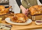 Three cooked turkeys on a kitchen countertop. A person is placing a turkey in a roasting pan onto the countertop.