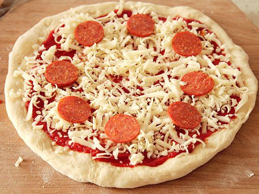 Pizza dough shaped into a round and topped with sauce, shredded cheese and pepperoni on a wood pizza peel, ready to go into the oven.