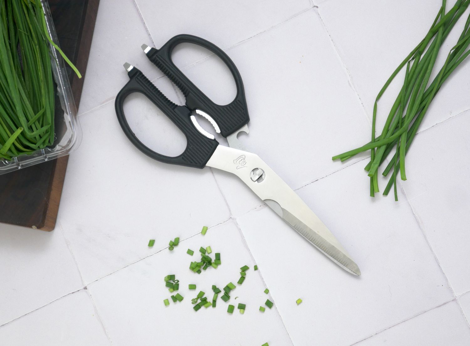shun kitchen shears on a white tile surface with snipped chives