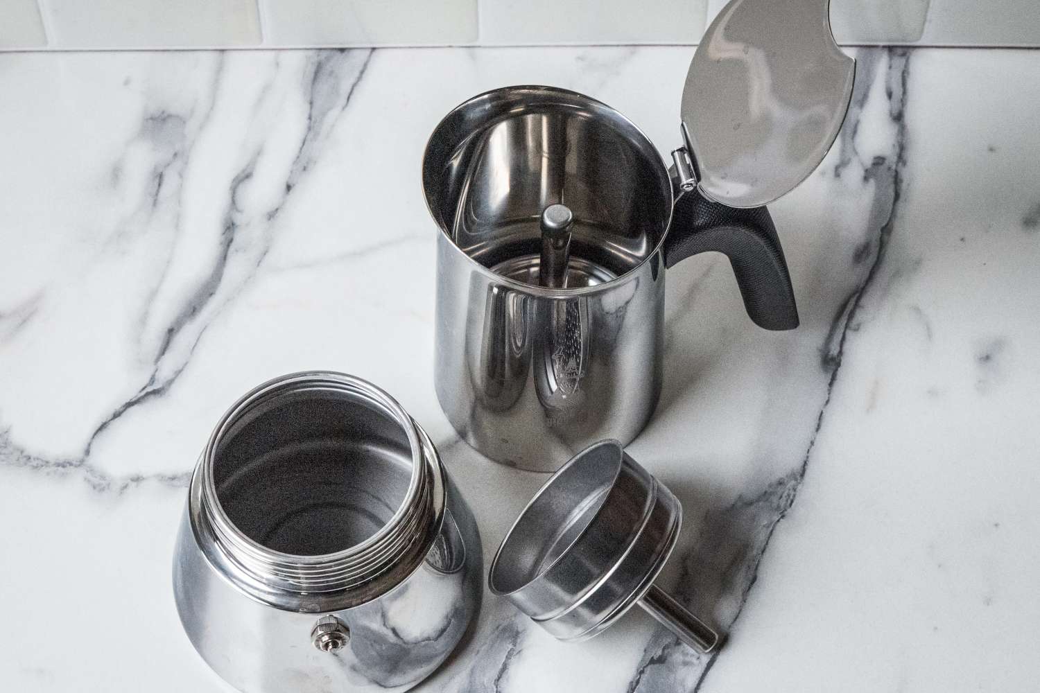Parts of a stovetop espresso maker shown disassembled on a marble countertop