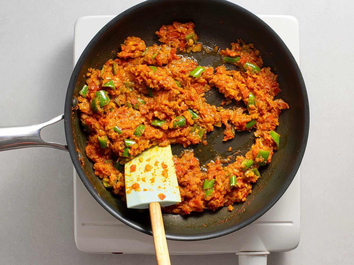 Green chiles, ginger-garlic paste, red chile powder, and turmeric powder being fried in a non-stick pan until oil separates from the paste.