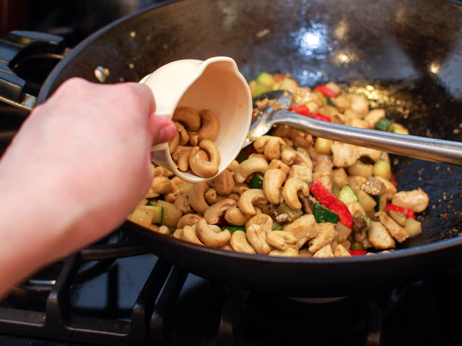 Adding cashews to cashew chicken ding in a wok.