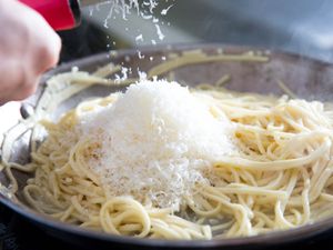 Showering grated cheese down into a skillet full of spaghetti