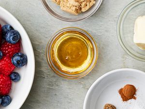 Ingredients for a recipe including honey in a small bowl berries sugar butter and spices arranged on a tabletop