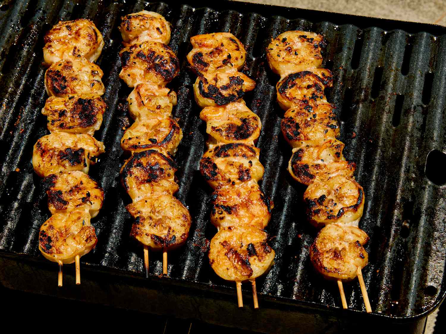 Four skewers of grilled shrimp on a barbecue grill