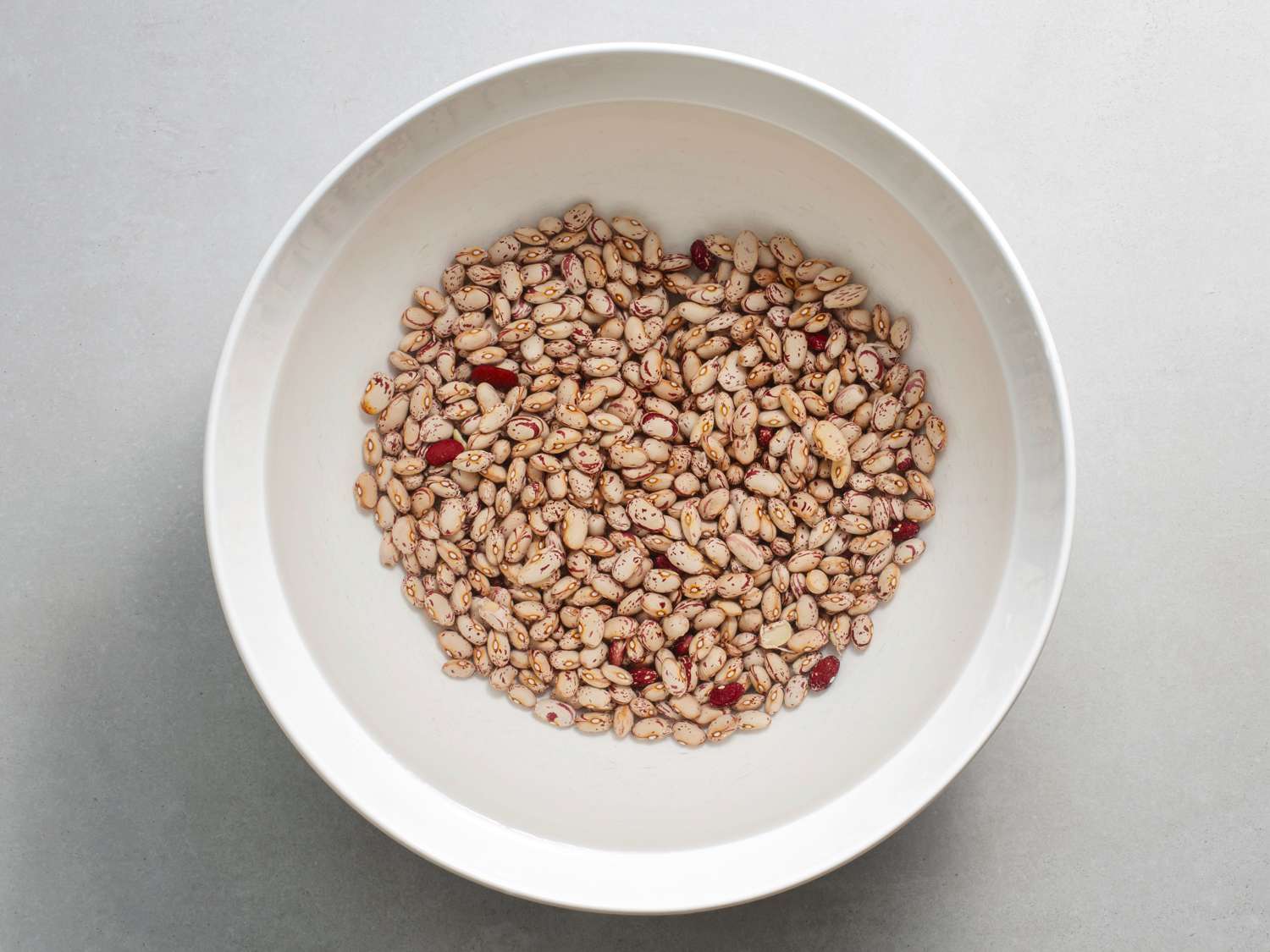 Pinto beans soaking in water in a white bowl.