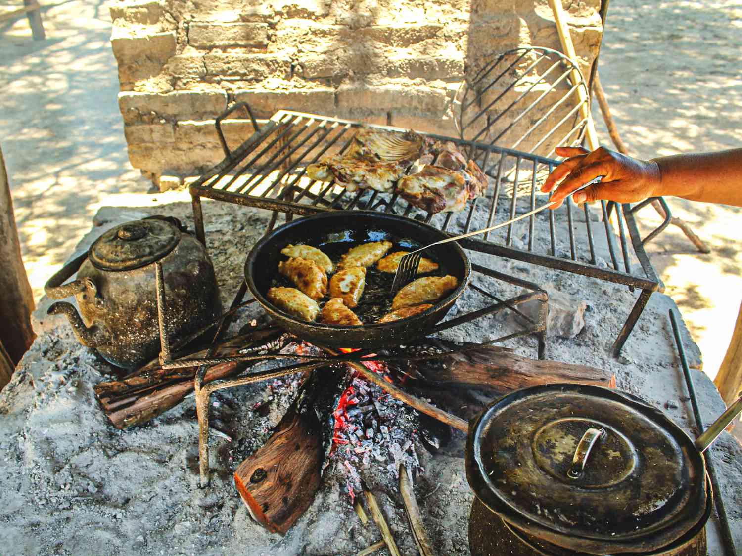 Goat empanadas being fried over live fire in an outdoor kitchen