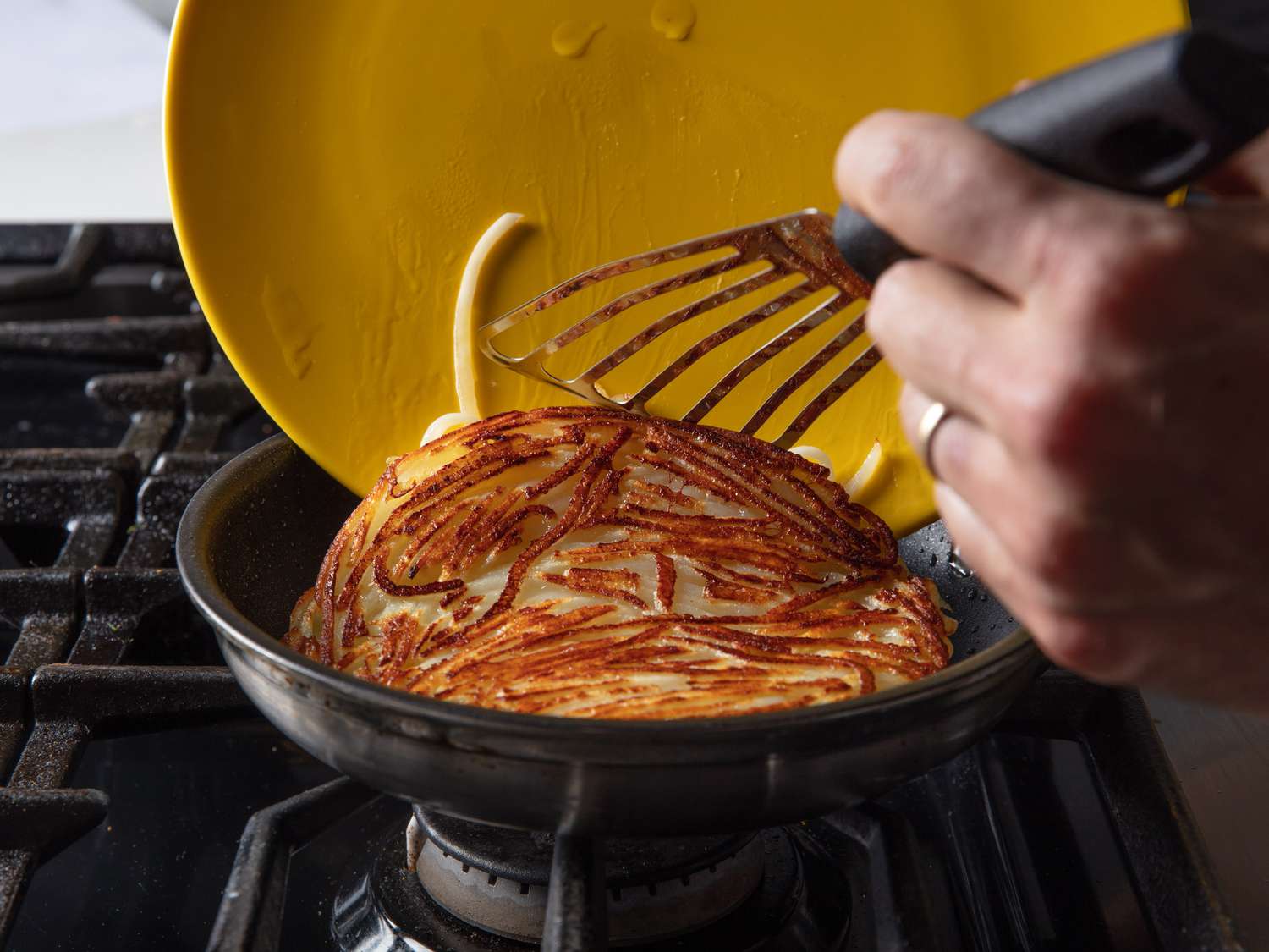 The pommes Darphin being slid from a plate back into the skillet to brown on its second side.