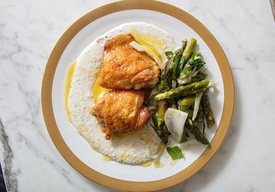 A plated dish with roasted chicken thighs, asparagus, and a creamy sauce