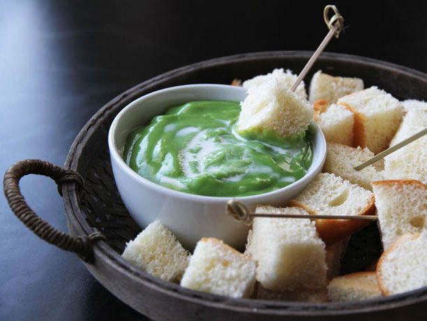 A bowl of Thai coconut dip set on a platter with cubes of bread and small skewers.