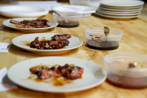 Multiple plates with meat on them next to containers of teriyaki sauces.