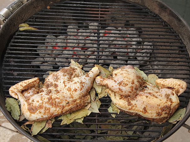 Jerk-marinated whole chicken halves grilling over bed of moist bay leaves over charcoal