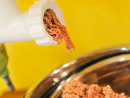 The ground sausage emerges from the meat grinding attachment of a stand mixer.