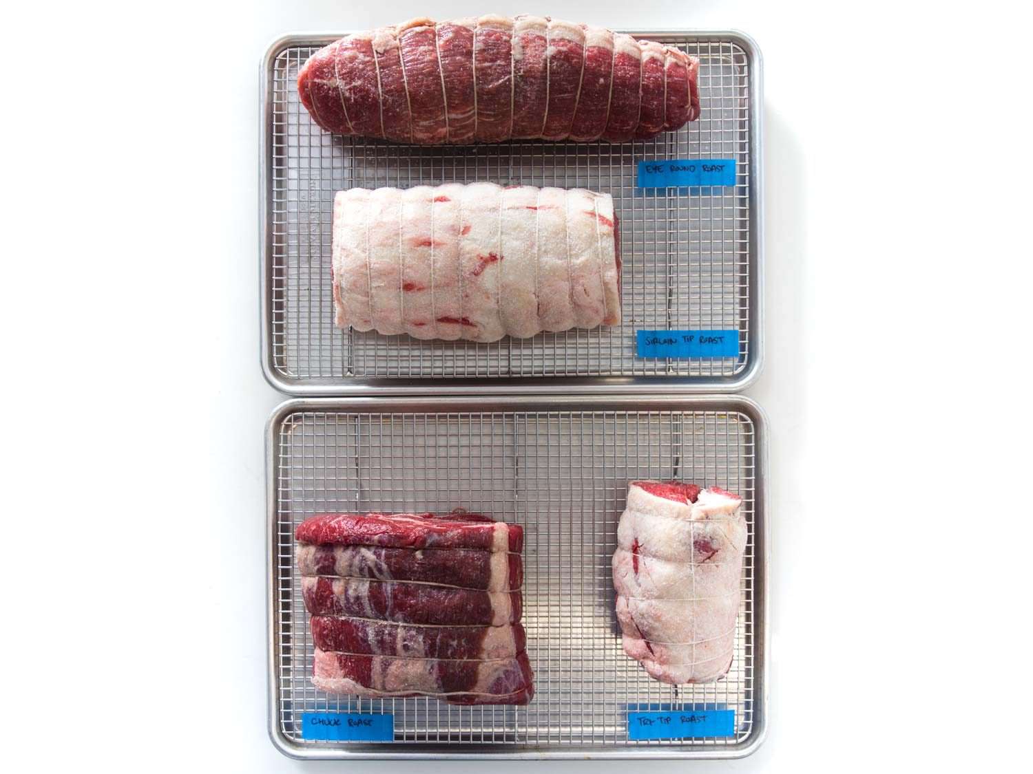 Overhead shot of four raw beef roasts: chuck, eye of round, top sirloin, and tri-tip.