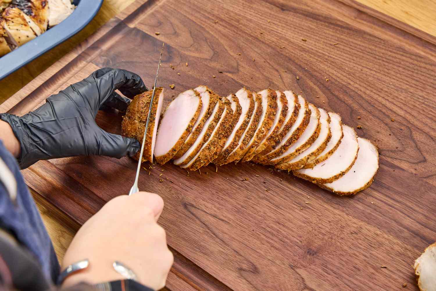 Sliced meat being cut on a Virginia Boys Kitchens Walnut Wood Cutting Board by a person wearing a glove