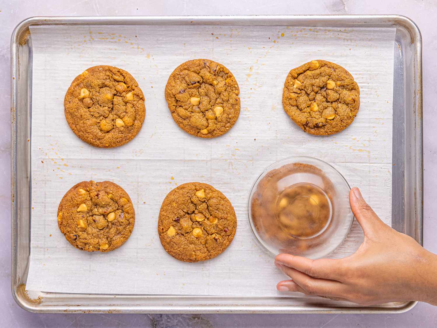 A person's hand pressing a glass on freshly baked cookies on a baking sheet lined with parchment paper