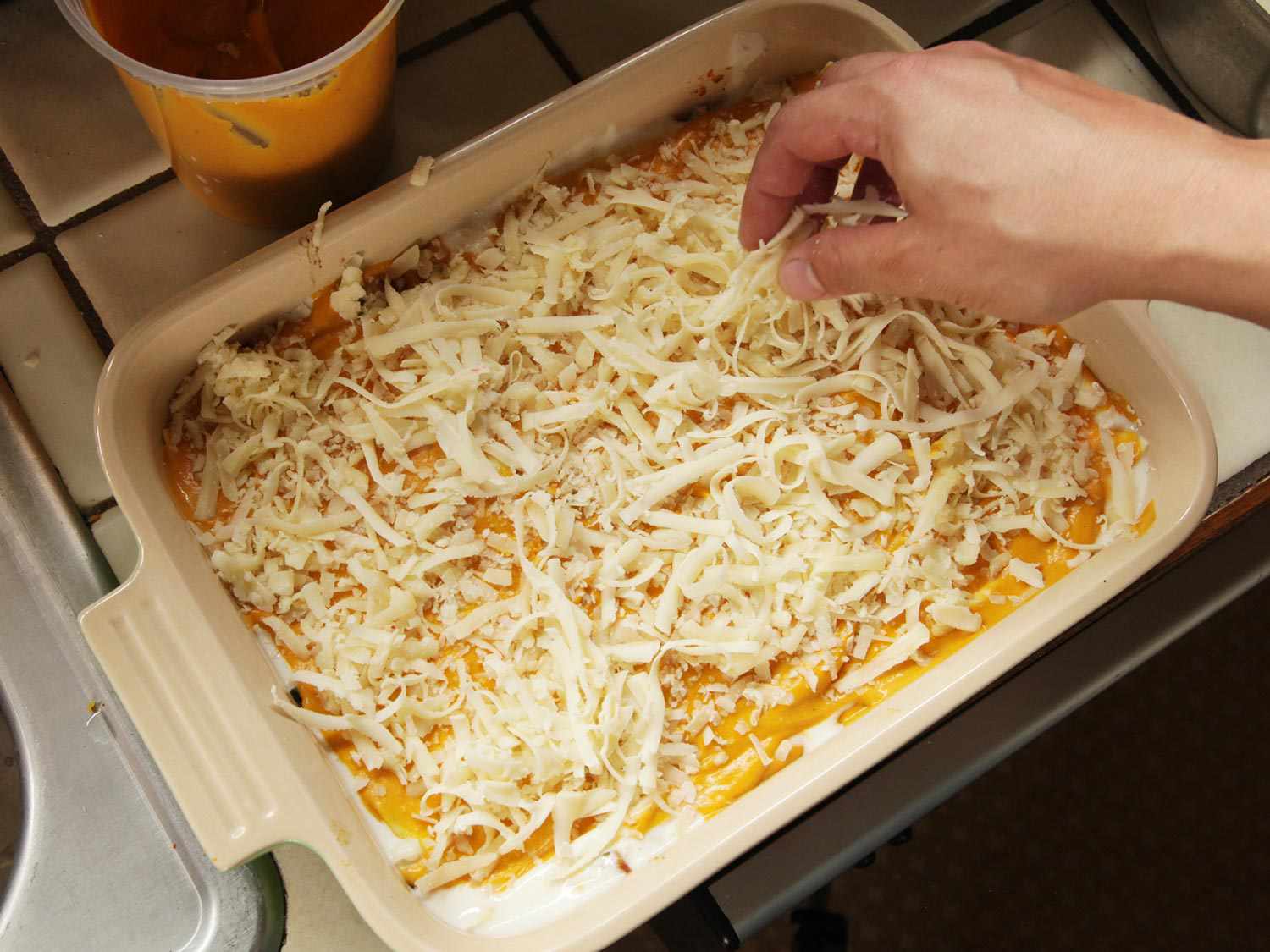 Sprinkling shredding cheese over squash lasagna filling.