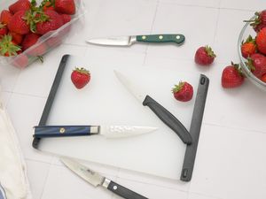 four paring knives on a white tile surface with strawberries