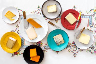 An assortment of cheeses, each on a separate plate with cheese knives.