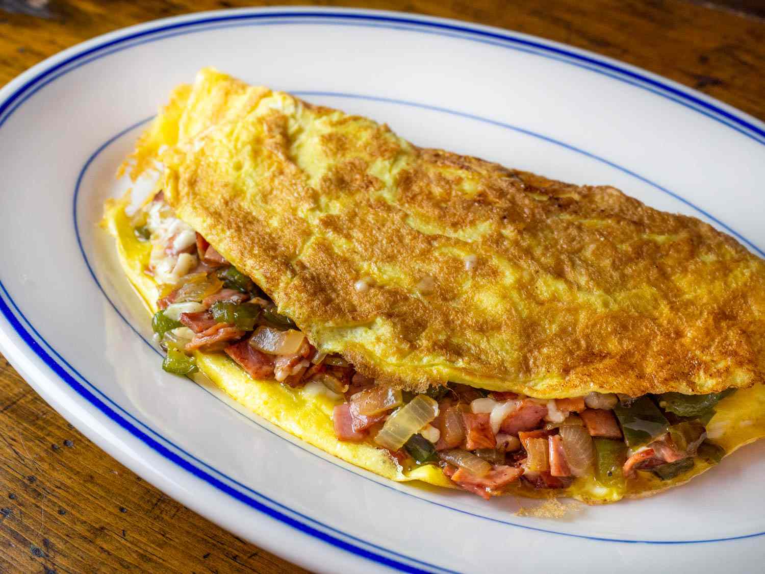 A large Western omelette stuffed with melted cheese and browned onions, peppers, and ham plated 