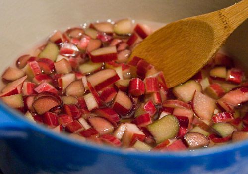 Chopped rhubarb cooking in a blue Dutch oven, with the rhubarb being stirred by a wooden spoon.