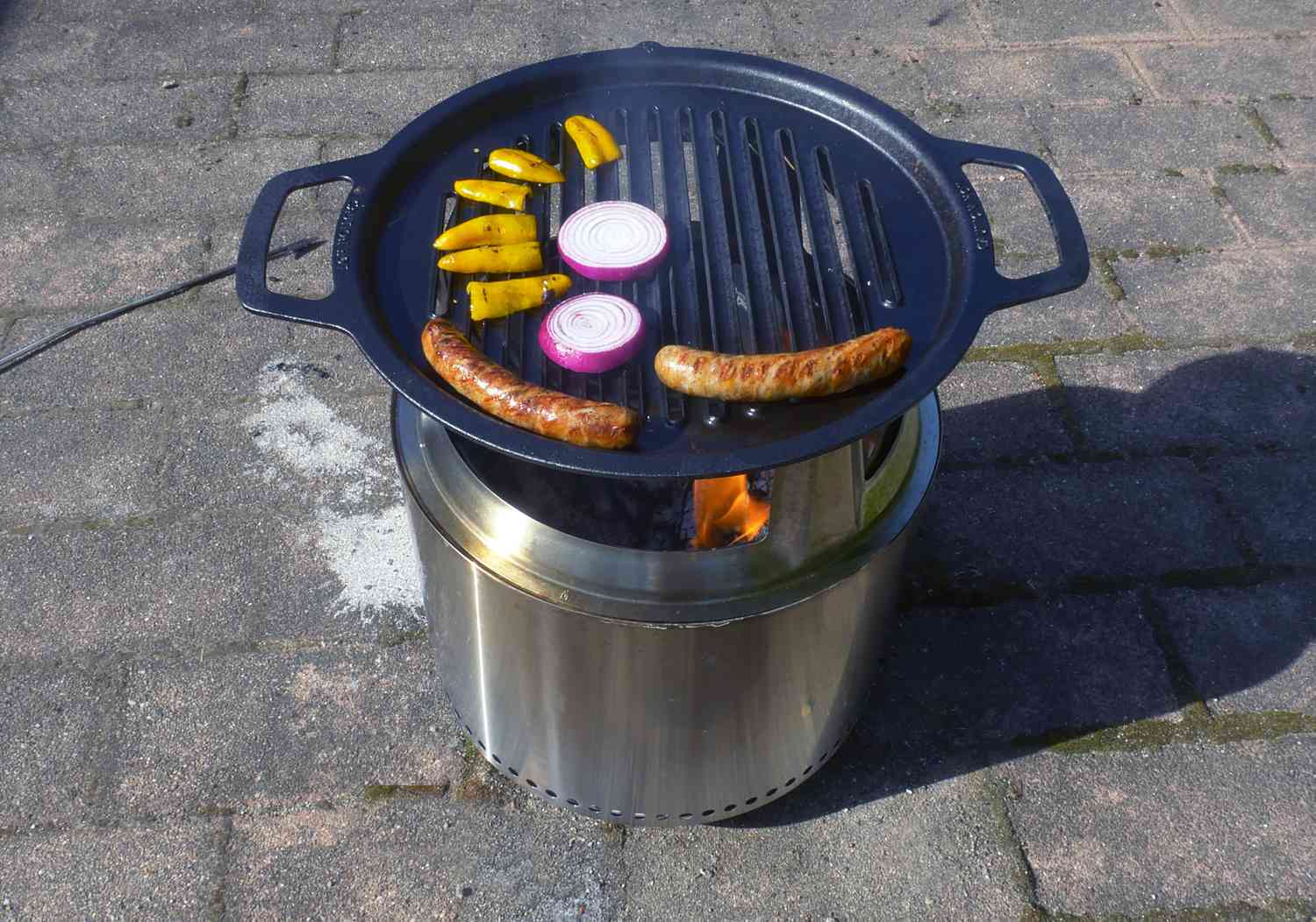 cooking italian sausages, red onion slices, and small sweet peppers on the solo stove with grill grate and hub