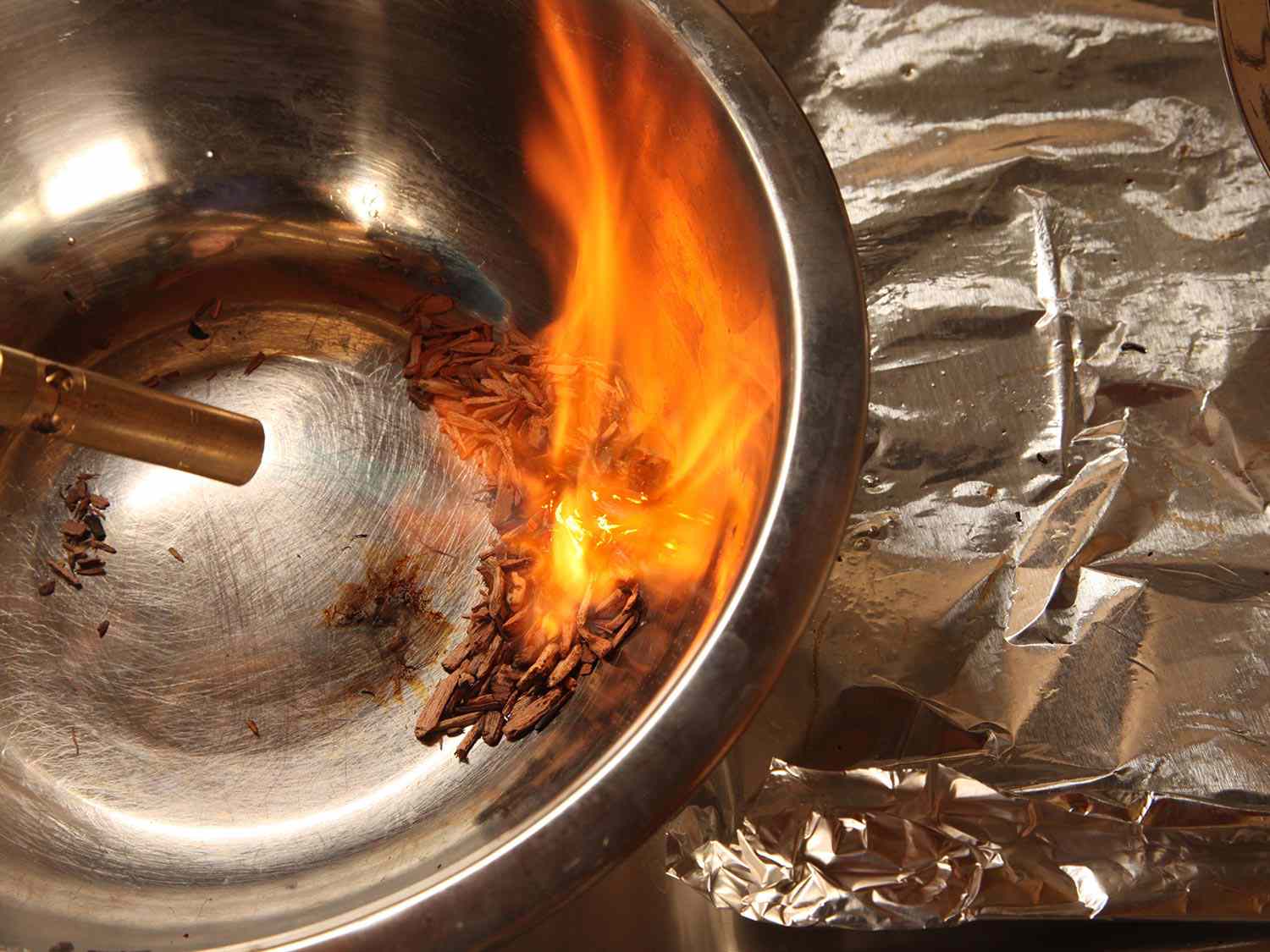Using a blowtorch to ignite wood chips in a metal mixing bowl.