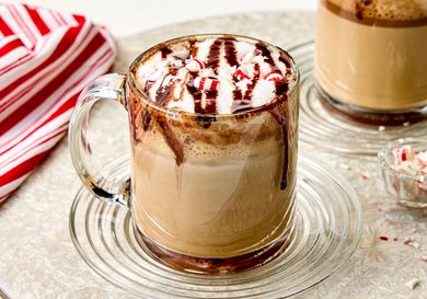 A mug of coffee topped with whipped cream chocolate drizzle and crushed peppermint candy