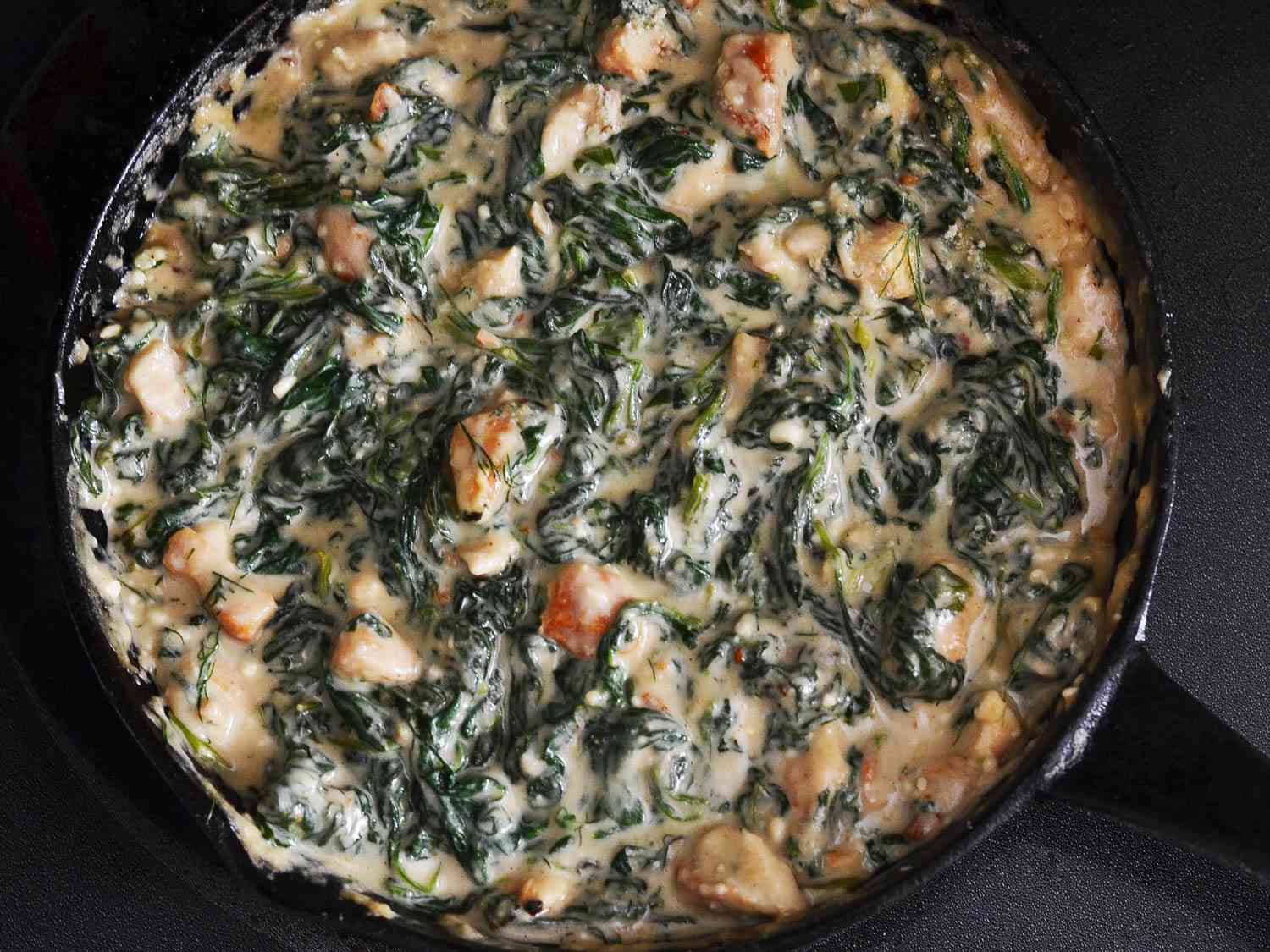 An overhead view of the chicken, spinach, and sauce combined in a skillet.