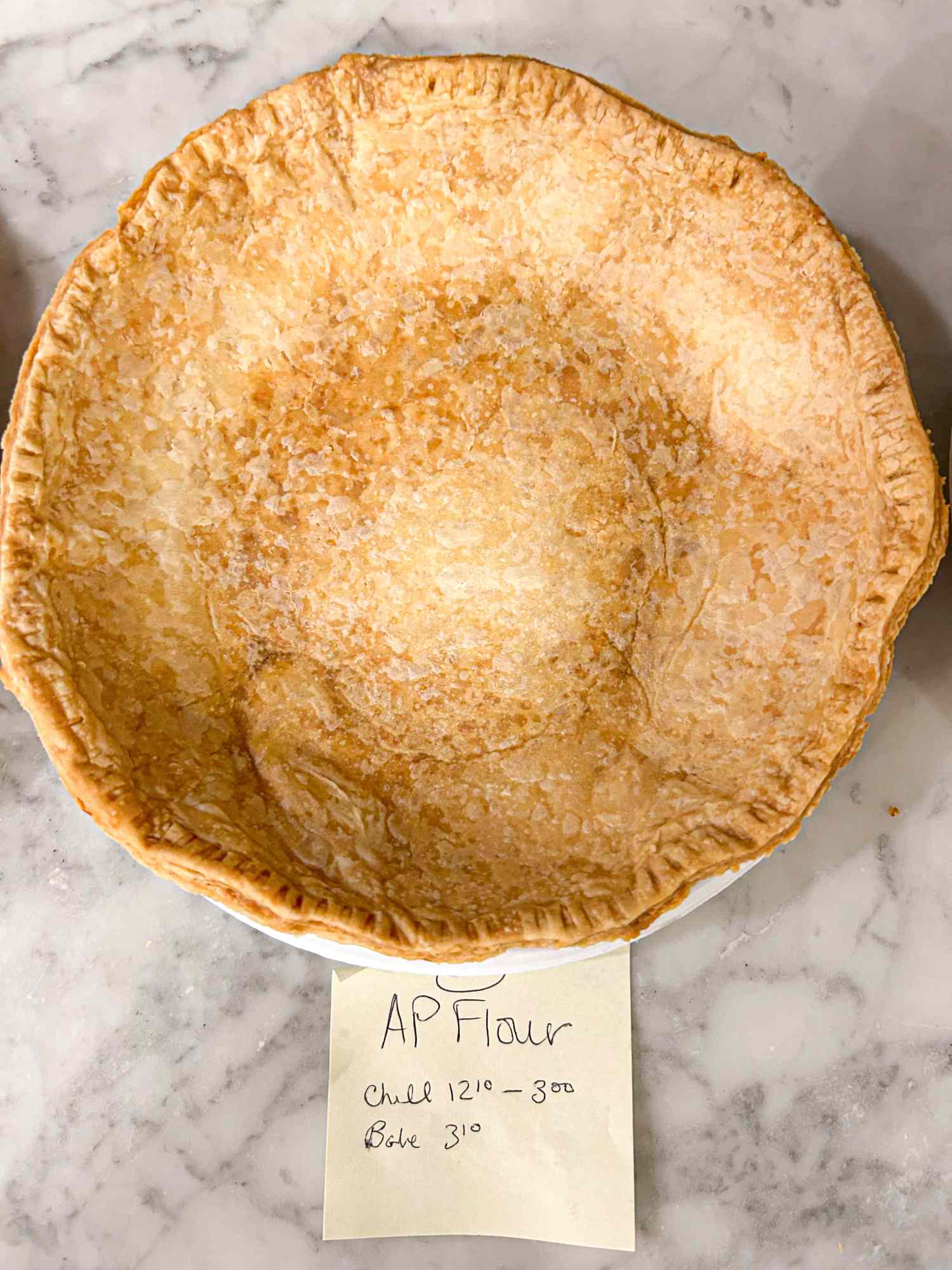 Baked pie crust in a dish labeled with a note describing the flour used and baking instructions