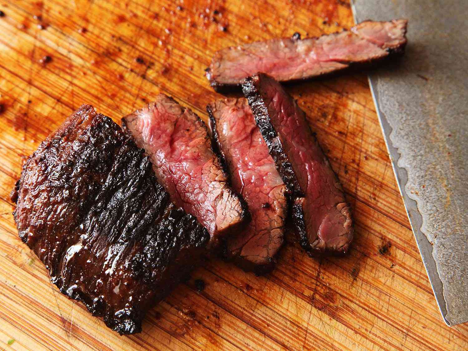 Slicing skirt steak carne asada against the grain on a wooden cutting board.