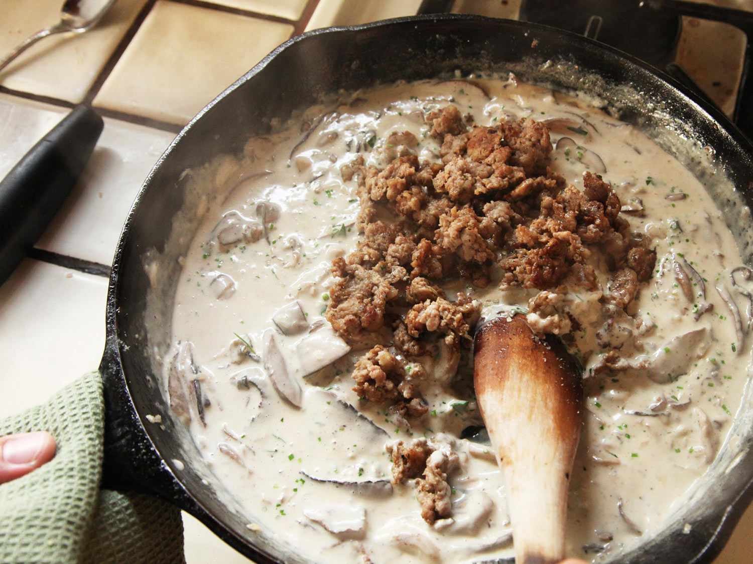 Adding cooked sausage meat back to mushroom cream sauce in a cast iron skillet. 