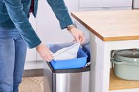 A person places a trash bag inside the simplehuman 38-Liter Brushed Stainless Steel Steel Trash Can with Lid