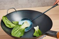 using a wok chuan to toss bok choy in a wok