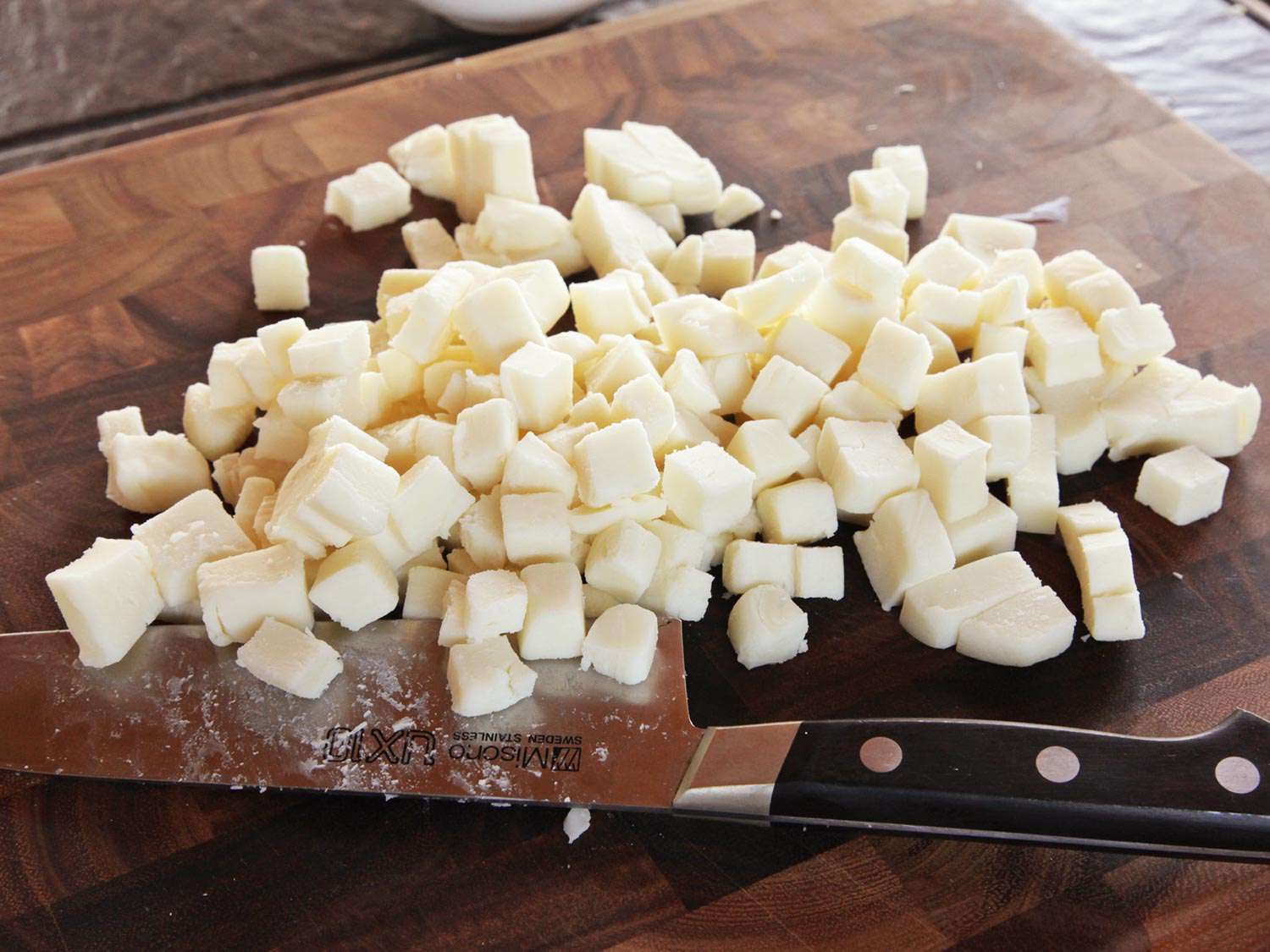 Cubes of low-moisture mozzarella cheese lying on a cutting board next to a chef's knife.