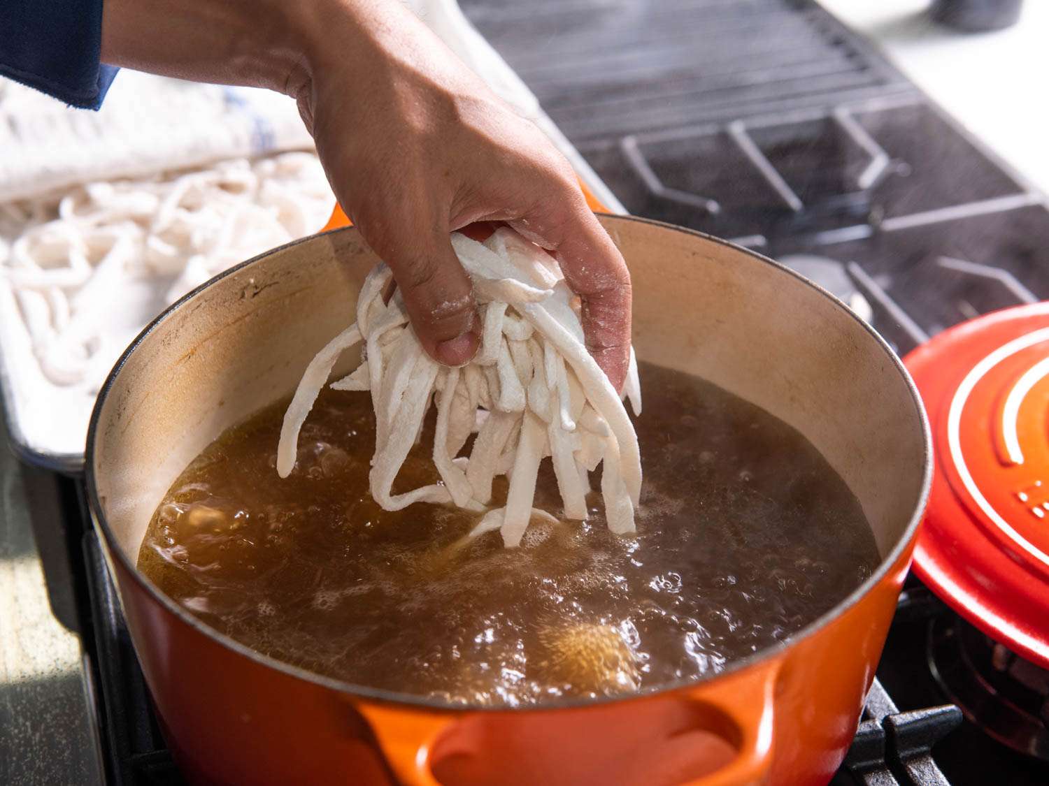 Adding raw noodles to broth for khao piak sen.