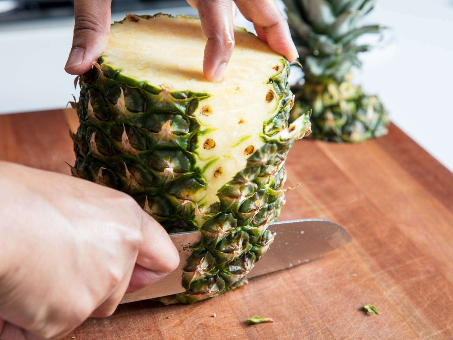 A knife slicing off the sides of a pineapple.