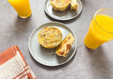 Two plates with muffin tin bacon egg bites next to glasses of orange juice