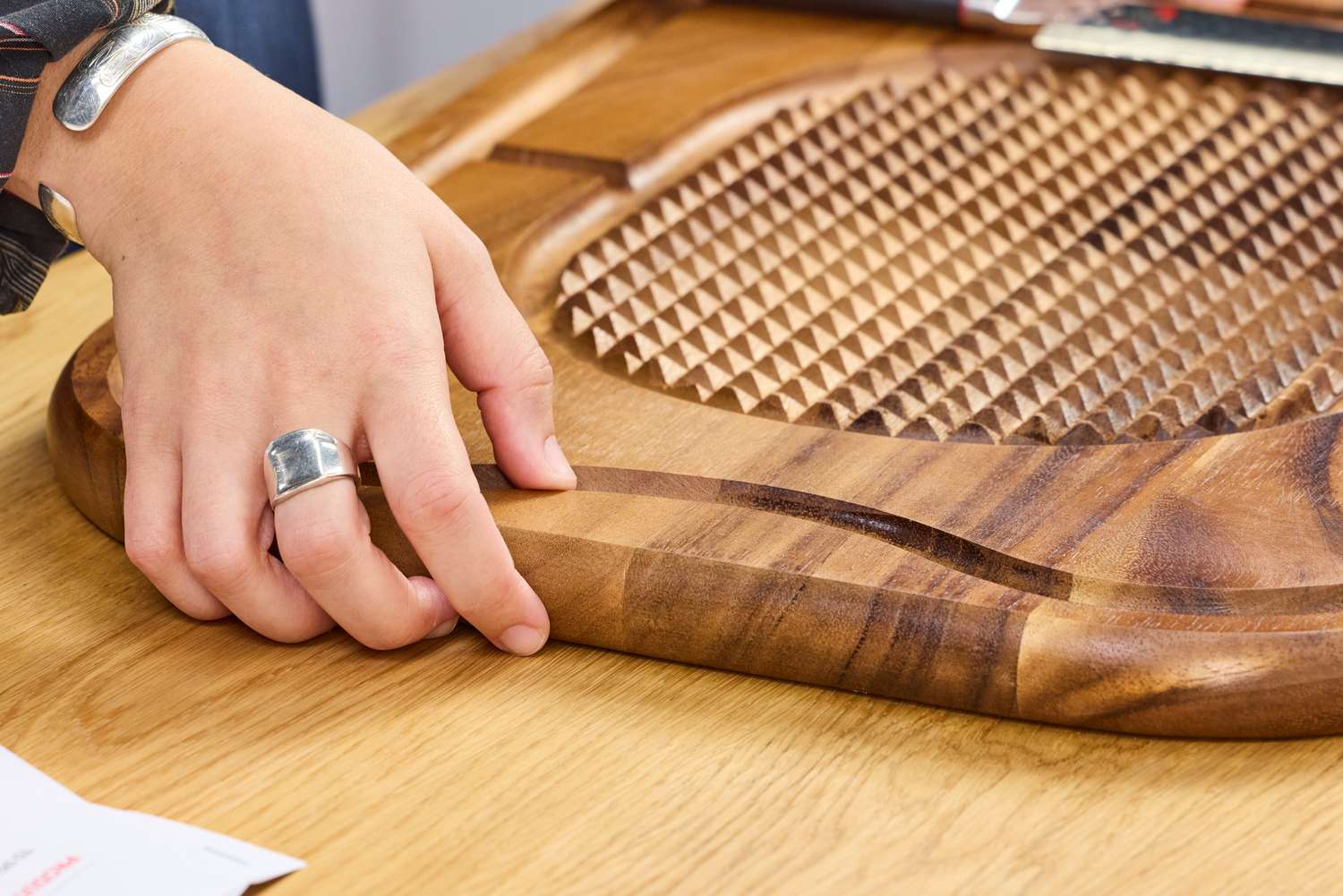 A person examining a Lipper International Acacia Cutting Board with Grid Grip with one hand placed on its edge