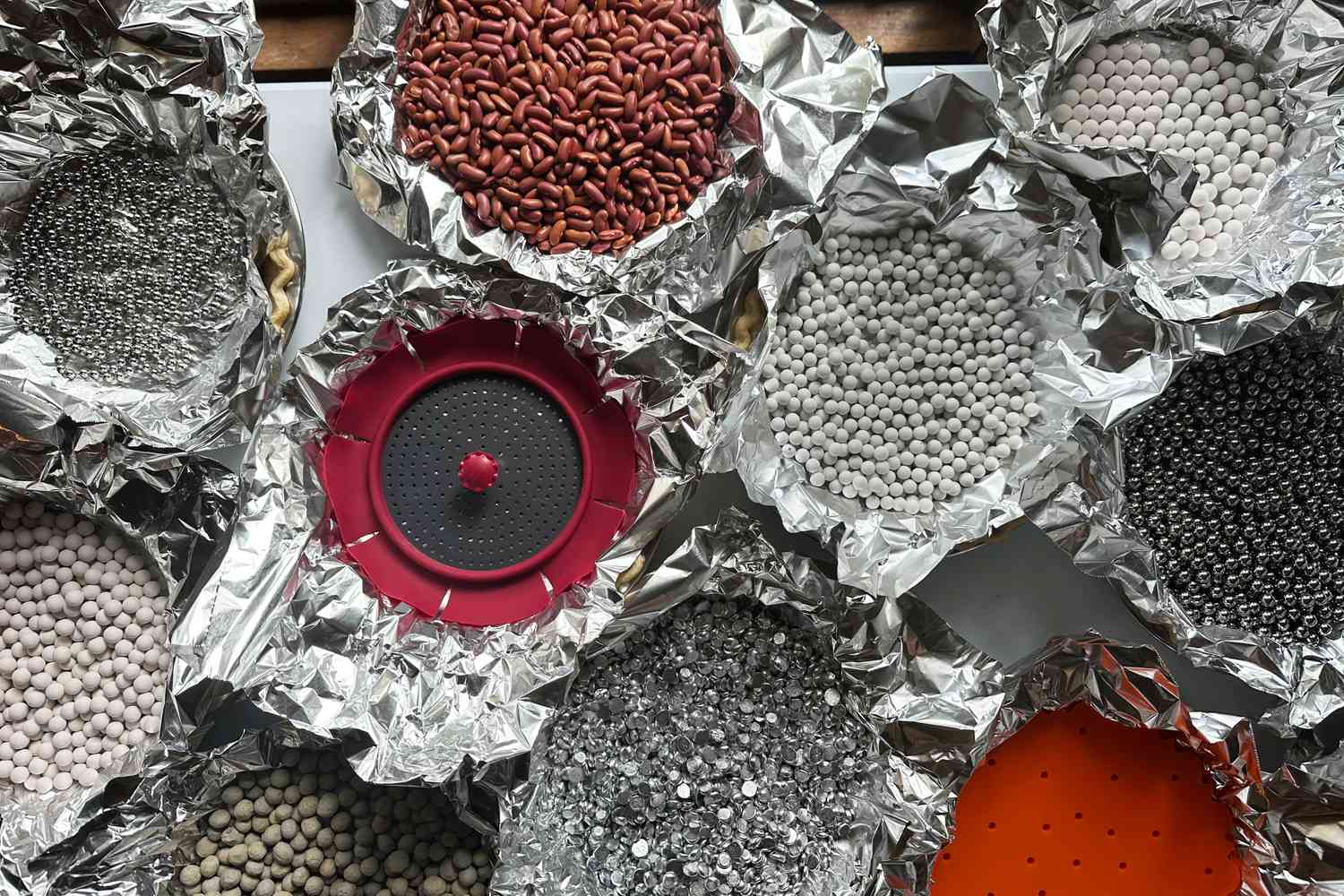 A collection of foil-lined pie shells, all covered with different styles of pie weights.