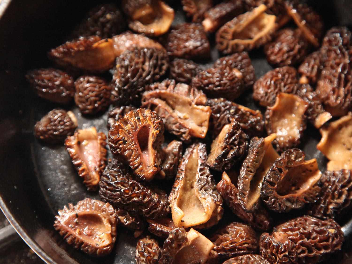 Close-up of morel mushrooms sautéing in a skillet.