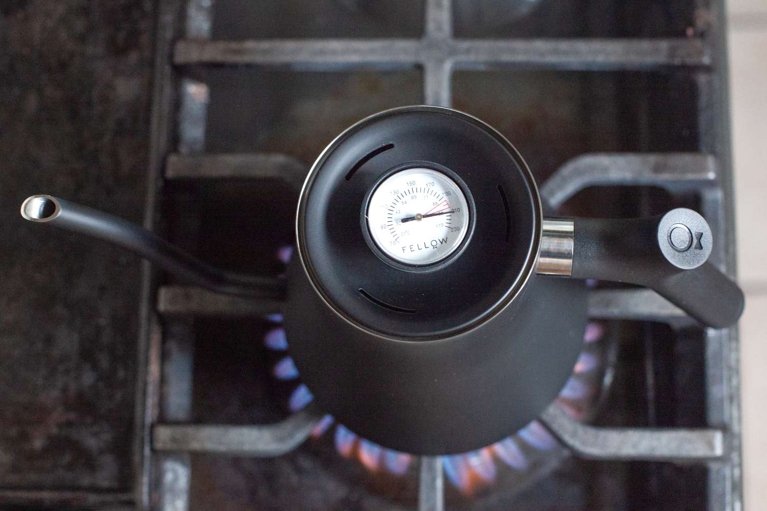 A gooseneck stovetop kettle with a thermometer dial placed on a lit gas burner