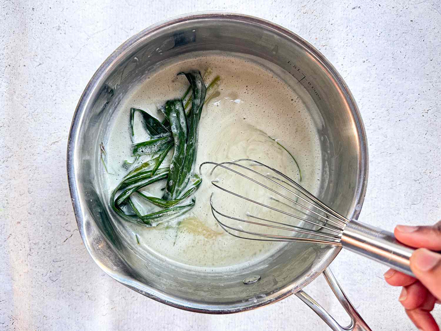whisking together sugar, pandan leaves, and coconut milk in a silver bowl 