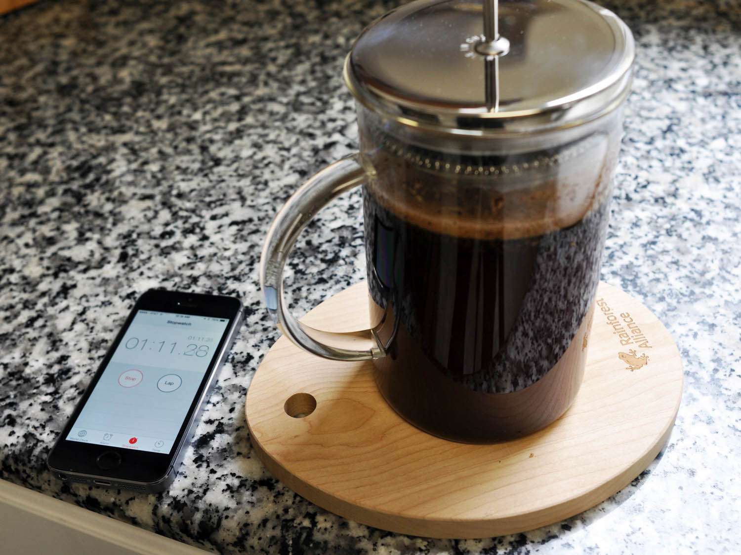 Coffee brewing in a glass French press with a phone with a count down timer off to the side.