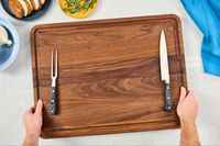 Hands holding a Virginia Boys Kitchens Walnut Wood Cutting Board with carving knife and fork