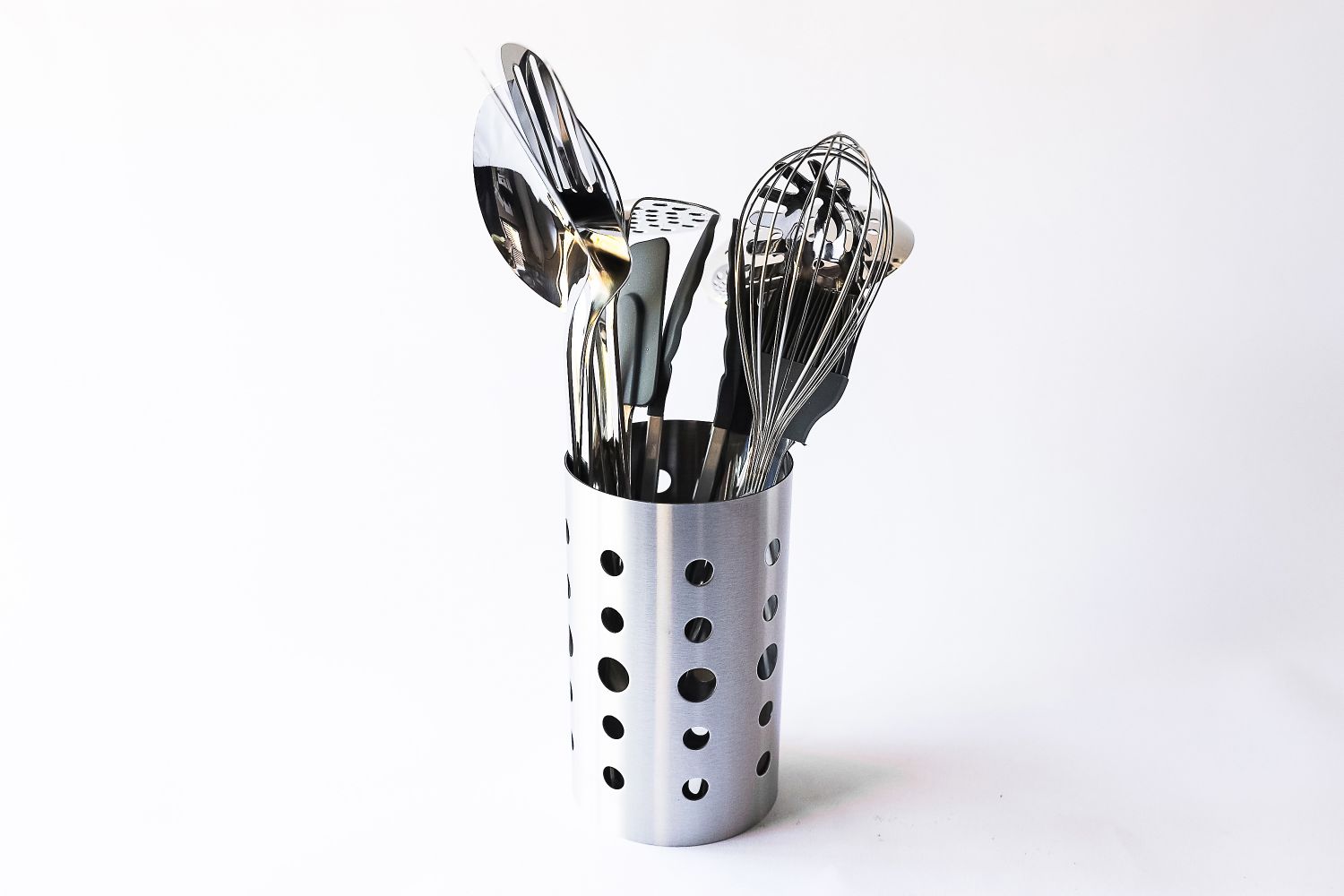 A metal utensil holder containing kitchen tools including a whisk spatula and spoon